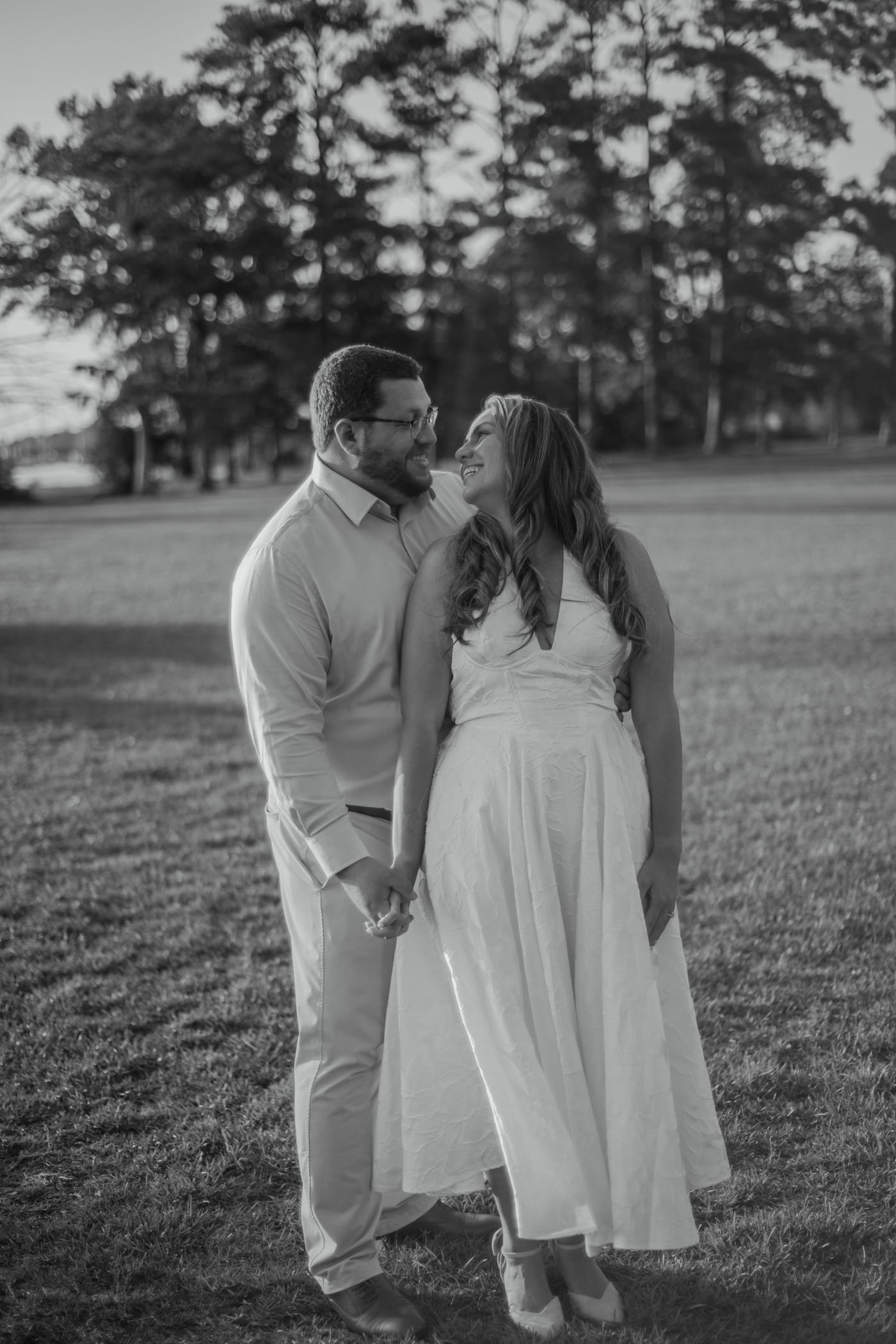 Black and white frame of the two of them holding hands and laughing in an open field.