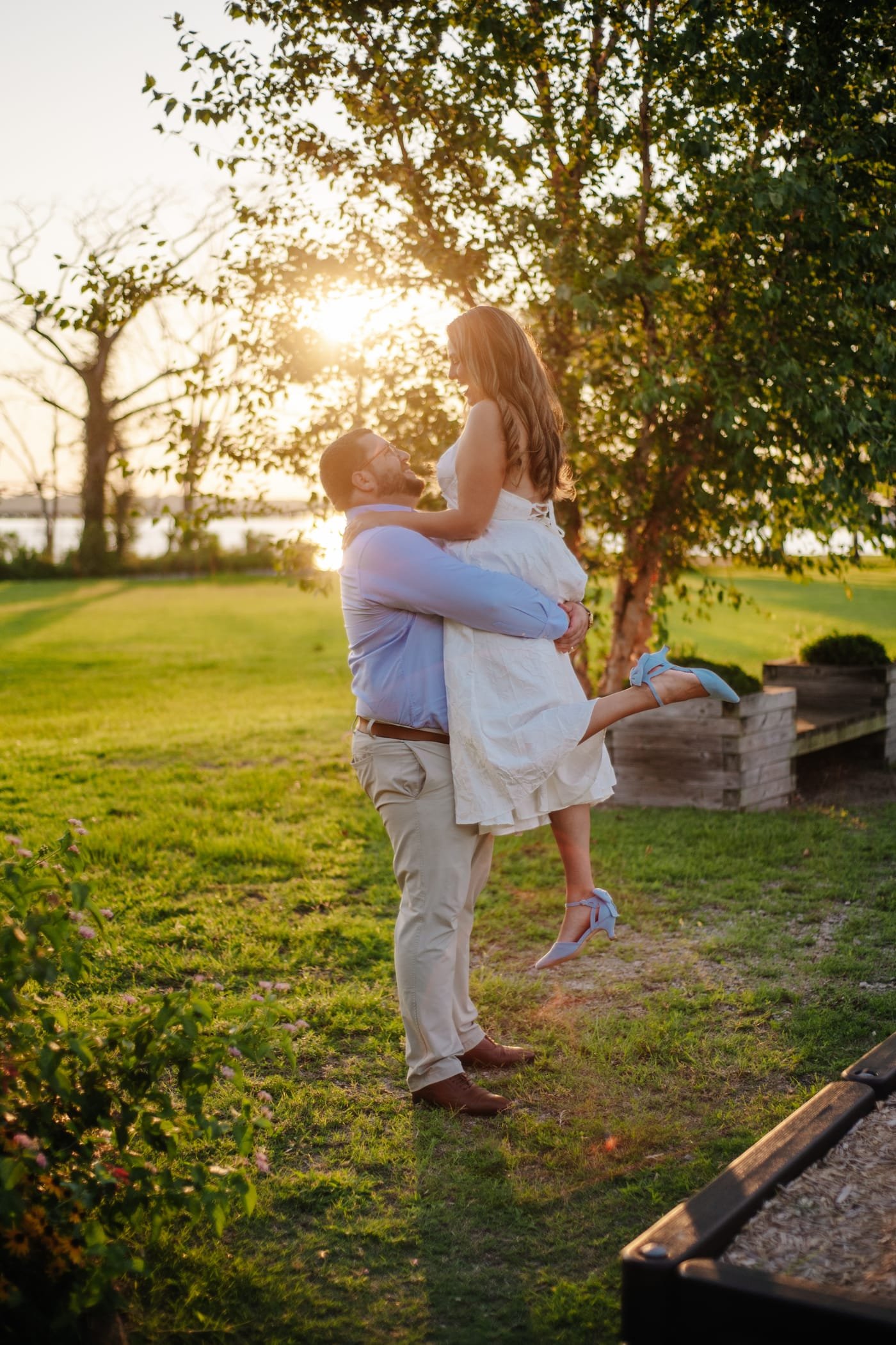 Pierce lifting Katherine off the ground with the sun setting behind the trees.